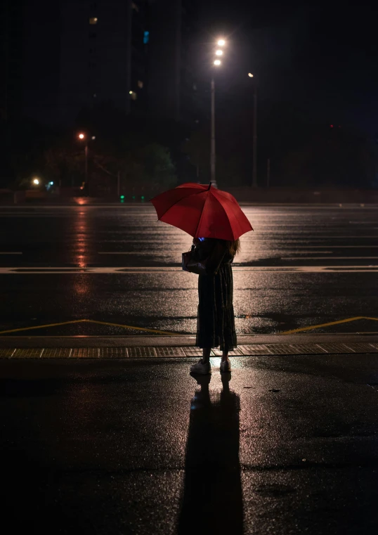 a person standing in the rain with a red umbrella, on a parking lot, in the evening