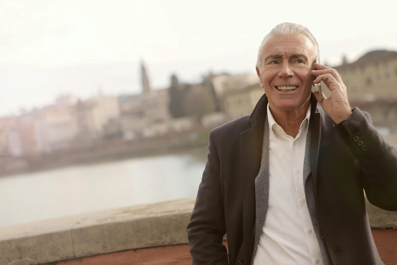 a man talking on a cell phone next to a river, by Giuseppe Avanzi, gray haired, 15081959 21121991 01012000 4k, looking happy, promo image