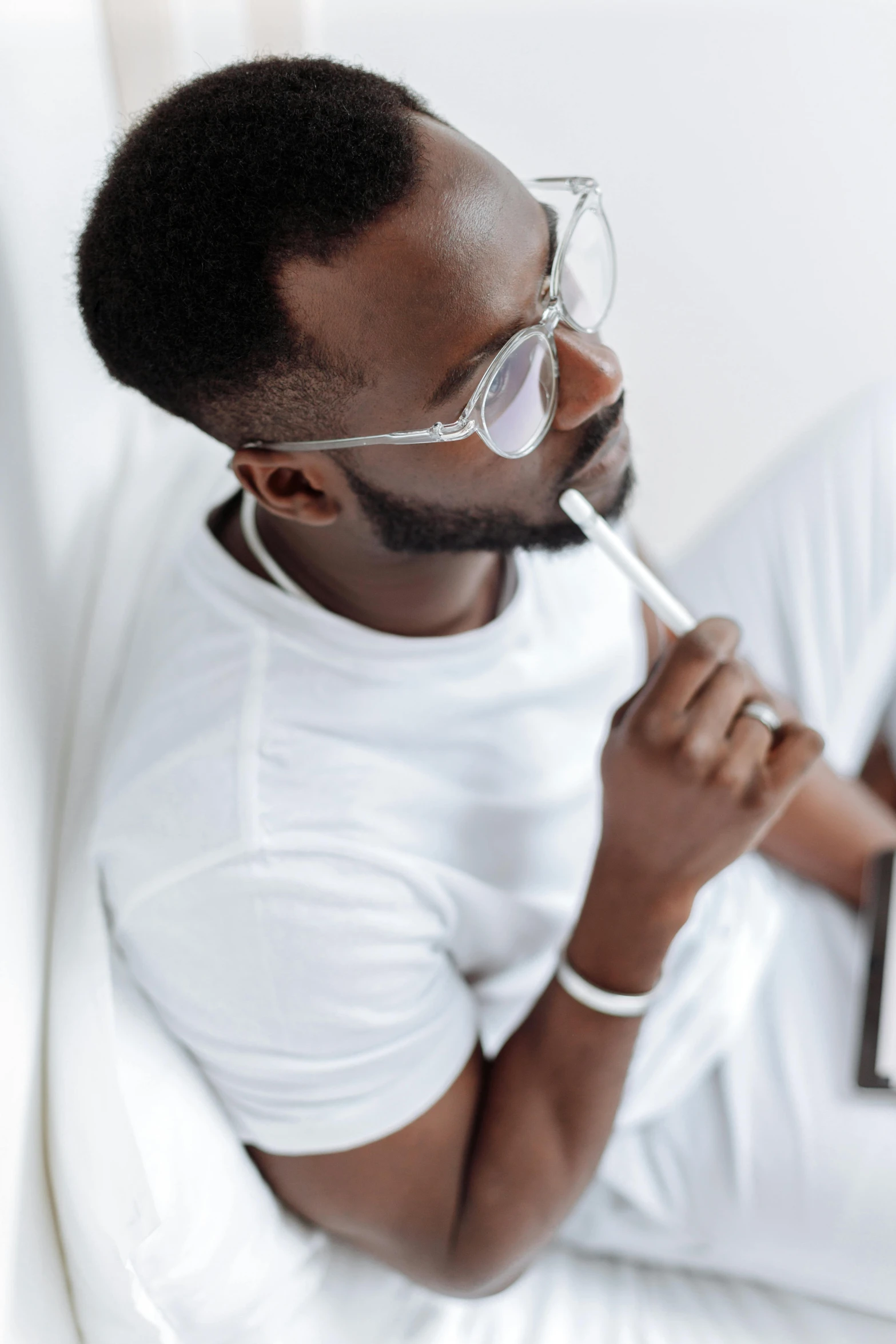 a man sitting on a bed using a laptop computer, an album cover, inspired by David Bailly, trending on pexels, white thick smoke, white glasses, holding pencil, ( ( dark skin ) )