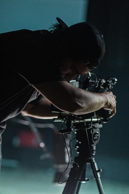 a man standing next to a camera on a tripod, inspired by roger deakins, performing on stage, maintenance, travis scott, getty images proshot