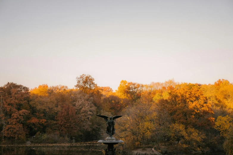 a fountain in the middle of a lake surrounded by trees, a statue, by Jesper Knudsen, unsplash contest winner, golden hour in manhattan, muted fall colors, winged victory, medium format. soft light