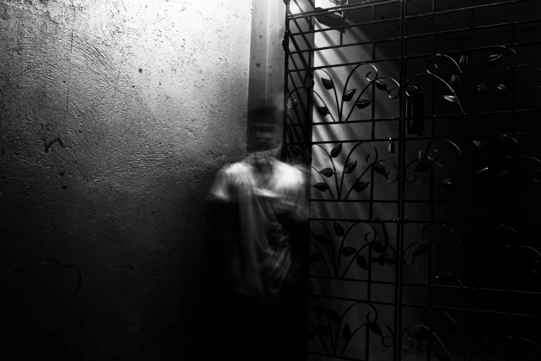 a black and white photo of a man leaning against a wall, conceptual art, enveloped in ghosts, behind bars, blurred face, uploaded