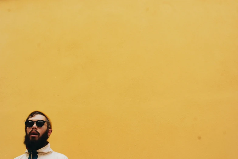 a man standing in front of a yellow wall, an album cover, pexels contest winner, postminimalism, bearded man, in white turtleneck shirt, pale orange colors, mac miller