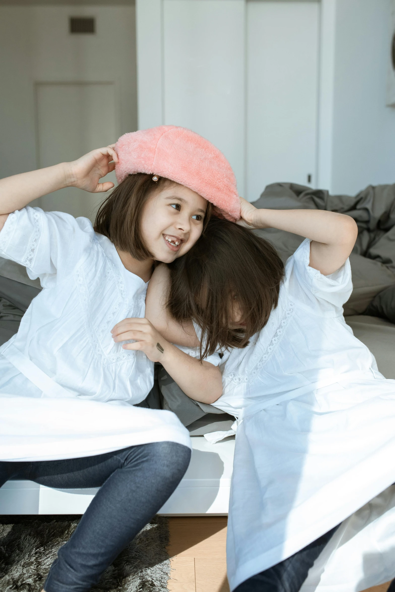 a couple of women sitting on top of a bed, inspired by Elsa Beskow, pexels contest winner, kids playing, an oversized beret, dressed in a white t shirt, close up angle