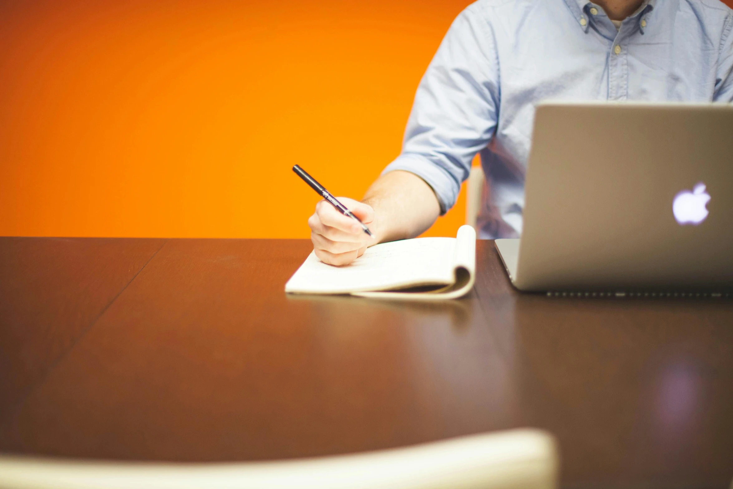 a man sitting at a table with a laptop and a notebook, by Jessie Algie, pexels, orange hue, whiteboards, royal commission, - signature