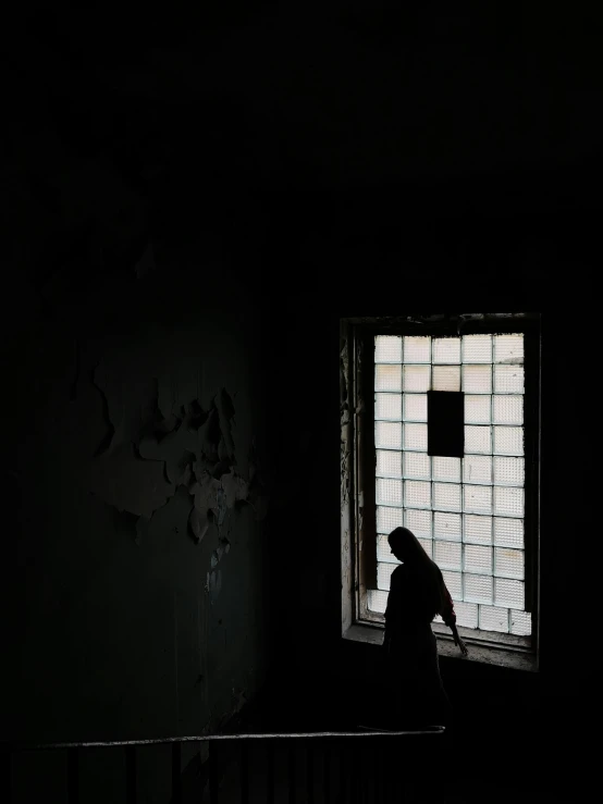 a person looking out a window in a dark room, standing in abandoned building, in prison, hila klein, silhouetted