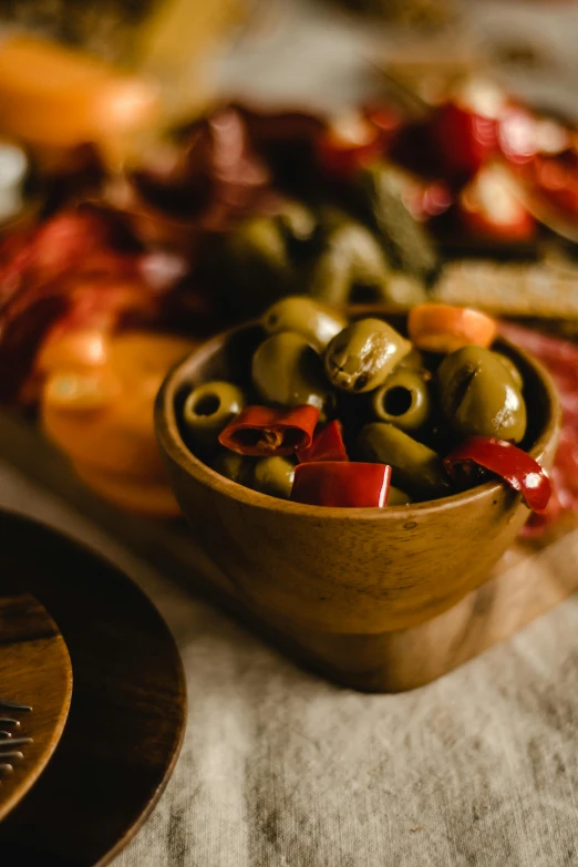 a wooden bowl filled with olives on top of a table, bowl filled with food, caparisons, snacks, 1 6 x 1 6