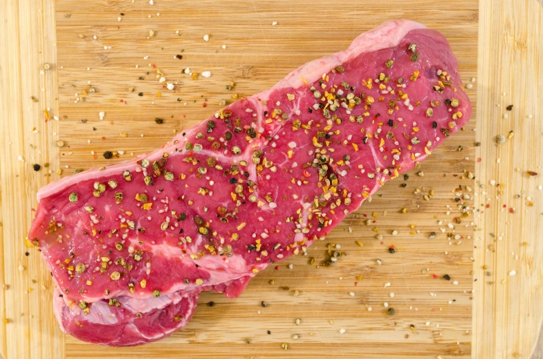 a piece of meat sitting on top of a wooden cutting board, gold speckles, pepper, full body image