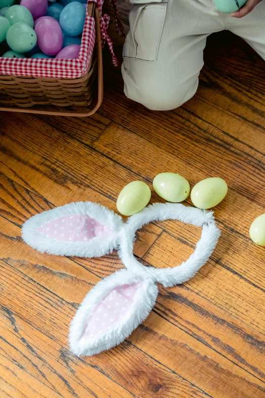 a child wearing bunny ears next to a basket of eggs, with tail, set pieces, up close, on a wooden table