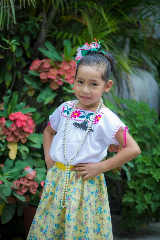 a little girl standing in front of a bush, inspired by Pacita Abad, pexels contest winner, wearing authentic attire, embroidered shirt, modeling for dulce and gabanna, square