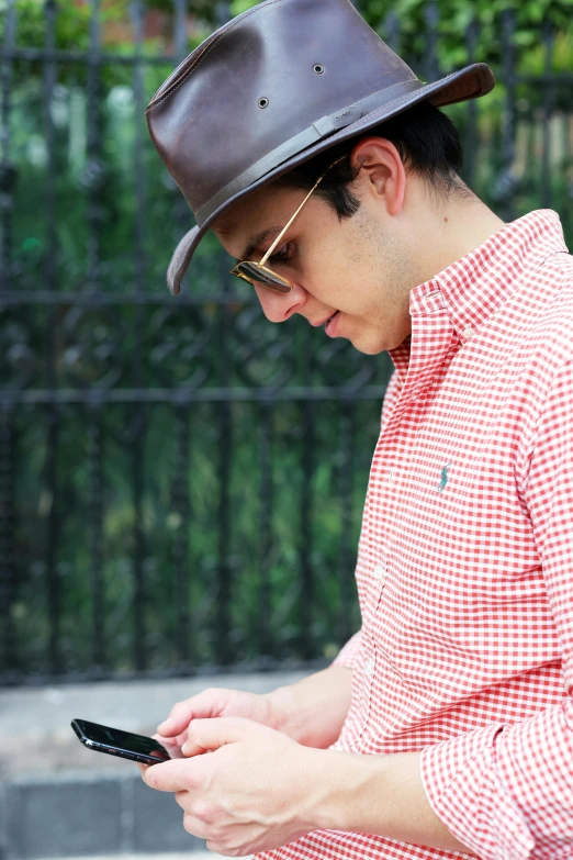 a man in a hat looking at his cell phone, an album cover, inspired by Alejandro Obregón, wearing plaid shirt, humans of new york style, profile image, dwell