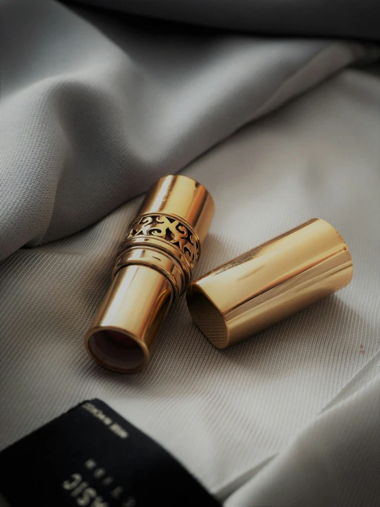 a gold lipstick sitting on top of a white shirt, pexels contest winner, hurufiyya, indonesia, scrolls, high quality product image”