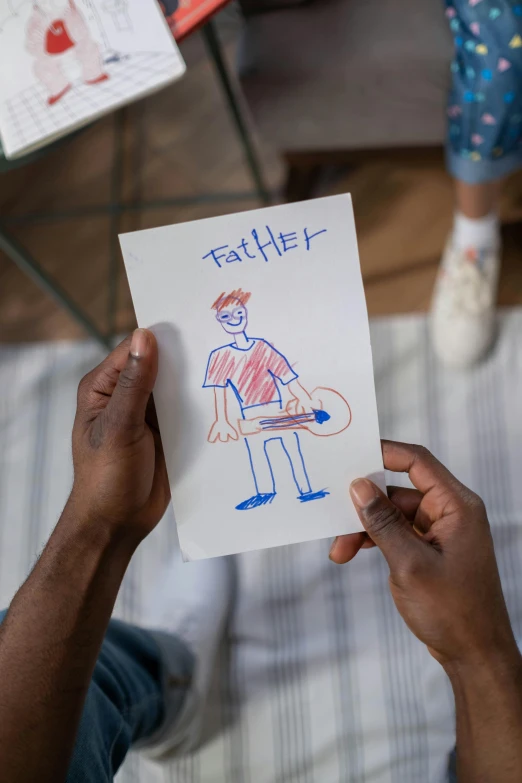 a person holding a piece of paper with a drawing on it, a child's drawing, by Paul Bird, fatherly, black teenage boy, dad bod, full scene shot