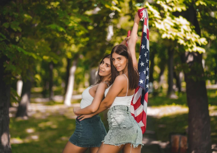 two women standing next to each other holding an american flag, a colorized photo, by Emma Andijewska, pexels contest winner, wearing a camisole and shorts, brunettes, adriana chechik, avatar image