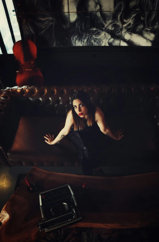 a woman sitting on a couch in a dark room, threatening pose, shot from above, promotional image, musician