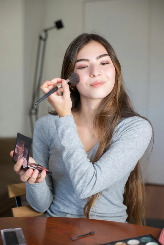 a woman sitting at a table doing makeup, by Robbie Trevino, photo product, college, slate, showing her face