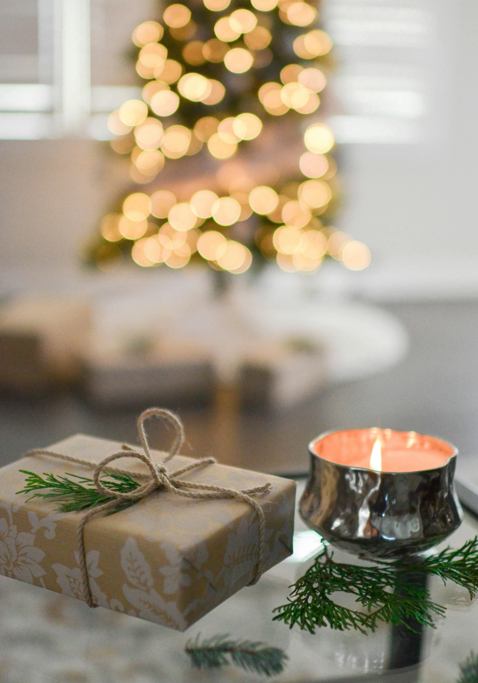 a present sitting on top of a table next to a christmas tree, candle lightning, profile image, candles, silver light