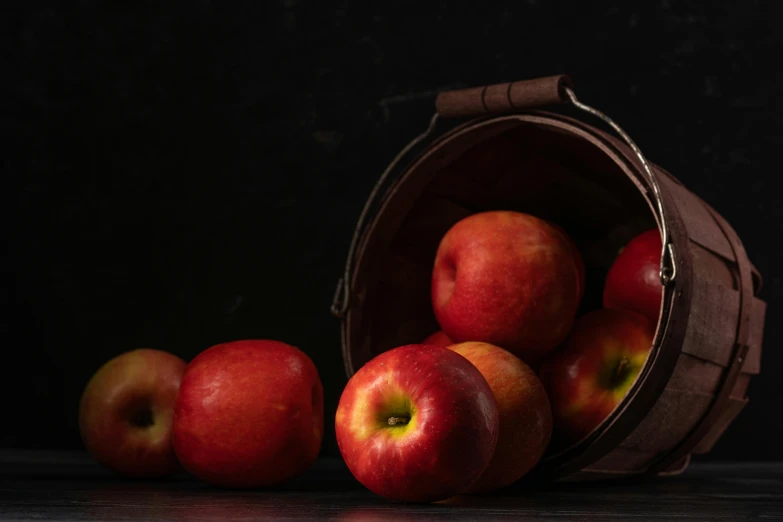 a bucket filled with red apples sitting on top of a table, on a dark background, shot with sony alpha 1 camera, round-cropped, ad image