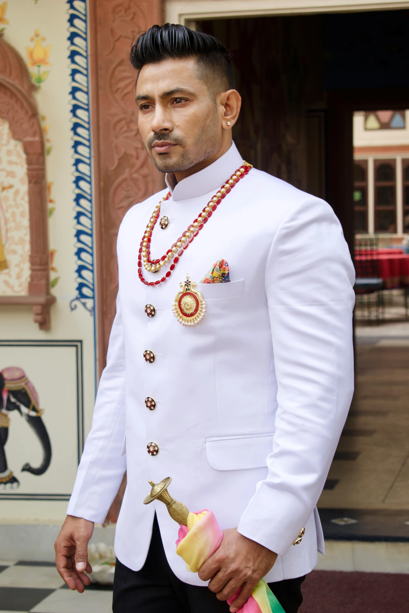 a man in a white suit standing in front of a building, inspired by Sardar Sobha Singh, renaissance, forehead jewelry, royal gown, profile image, dragon - inspired suit