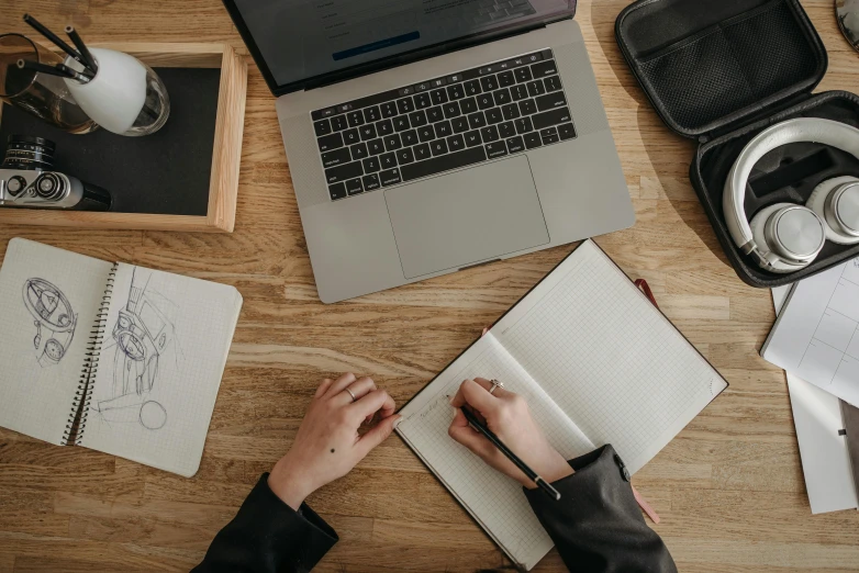 a person sitting at a desk working on a laptop, pexels contest winner, pen and paper, 9 9 designs, a wooden, holding notebook