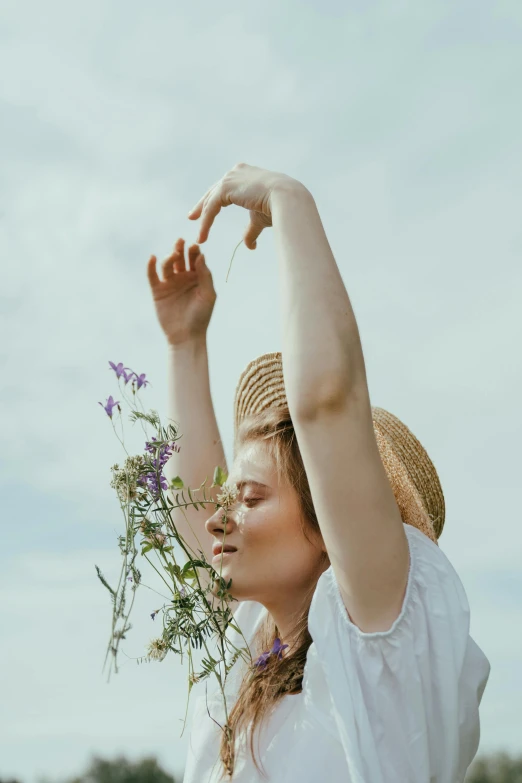 a woman standing in a field holding a bunch of flowers, trending on pexels, aestheticism, with branches! reaching the sky, woman with hat, portrait of elle fanning, hands shielding face