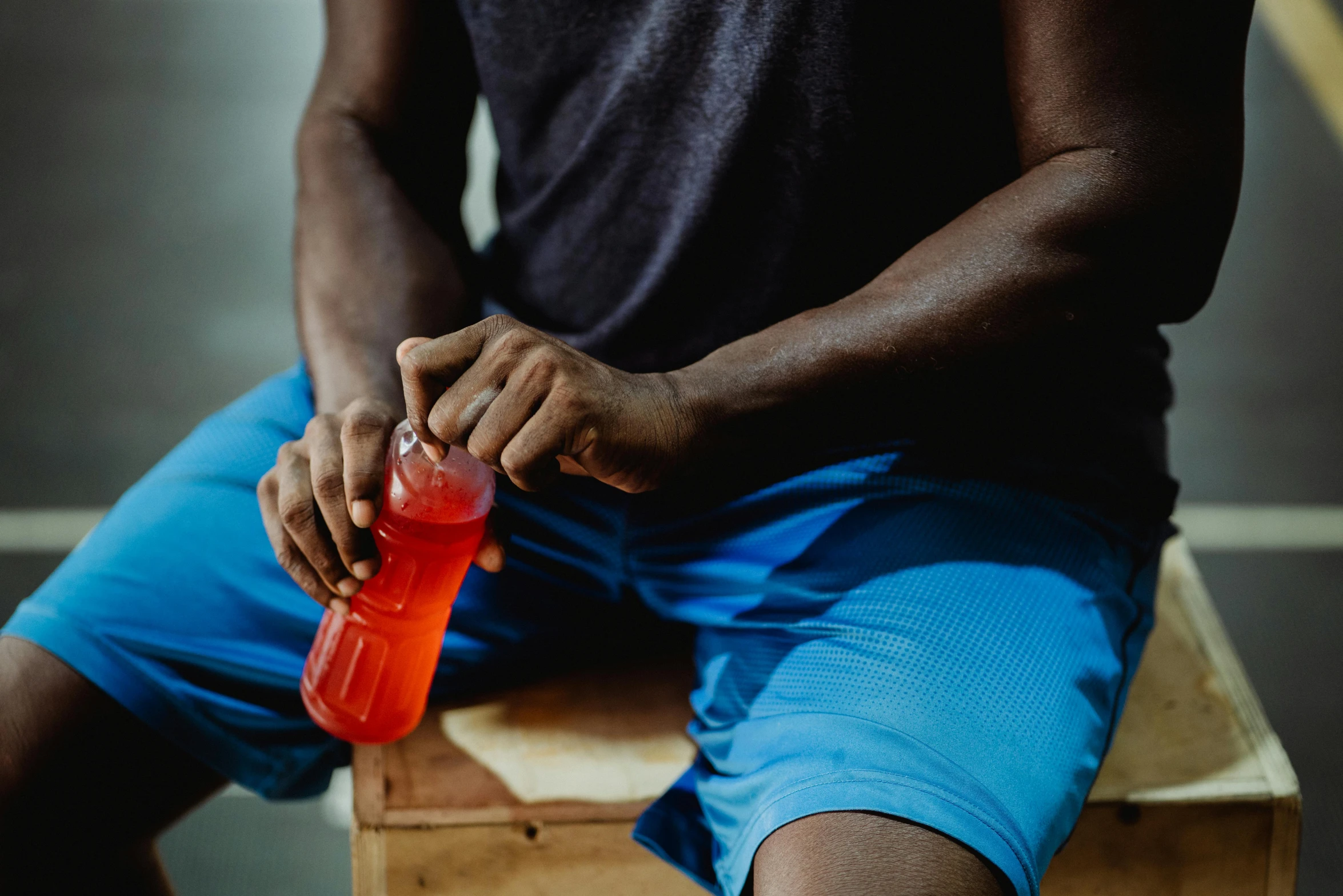 a man sitting on a bench holding a bottle of water, wearing red shorts, juice, zoomed in, high quality product image”