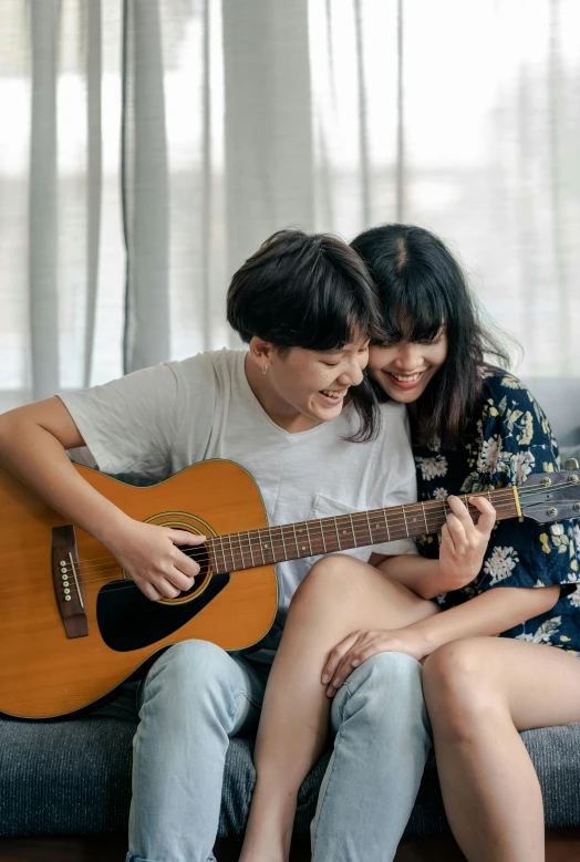 a man and woman sitting on a couch playing a guitar, pexels contest winner, asian female, hey buddy, loving embrace, charts