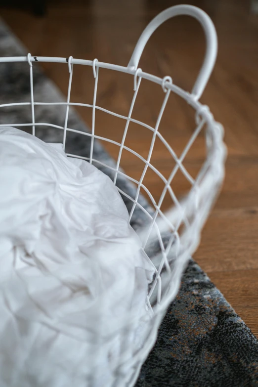 a white basket sitting on top of a wooden floor, swirling fabric, close - up photograph, iron, product shot