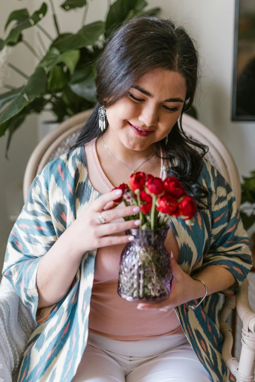 a woman sitting in a chair holding a vase of flowers, inspired by Maryam Hashemi, instagram, joyful look, partially cupping her hands, profile image, crimson accents