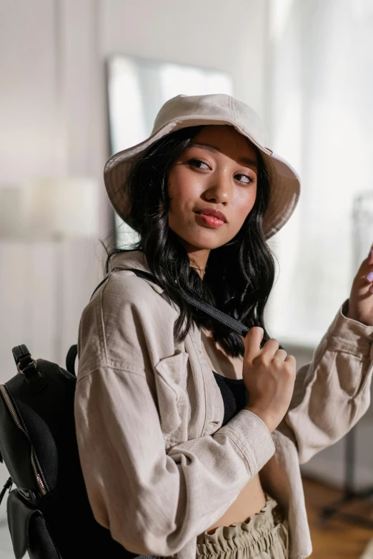 a woman wearing a hat and holding a cell phone, beige hoodie, mai anh tran, with a backpack, lily frank