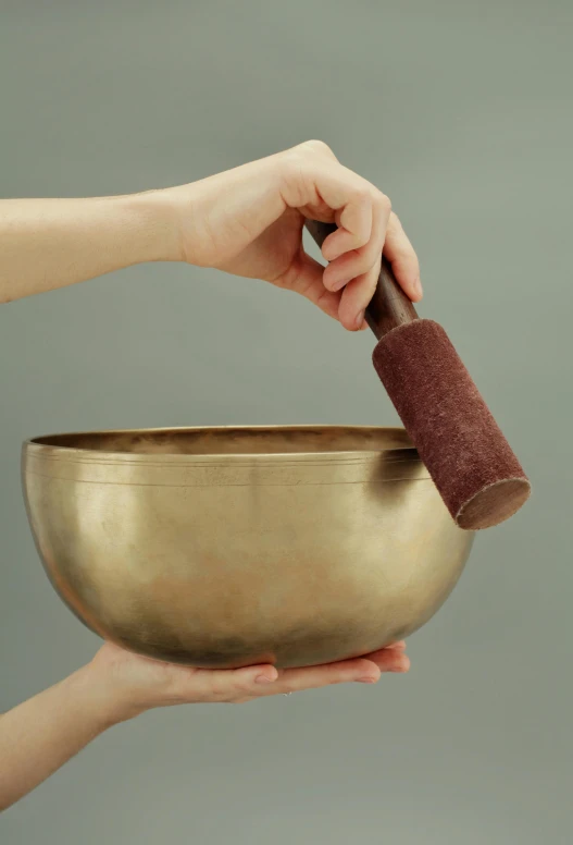 a person holding a singing bowl in their hand, ultra smooth, made in bronze, holding brush, vibrating