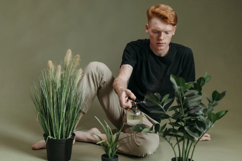 a man sitting on the ground next to a potted plant, ginger hair with freckles, pouring, curated collection, professional image
