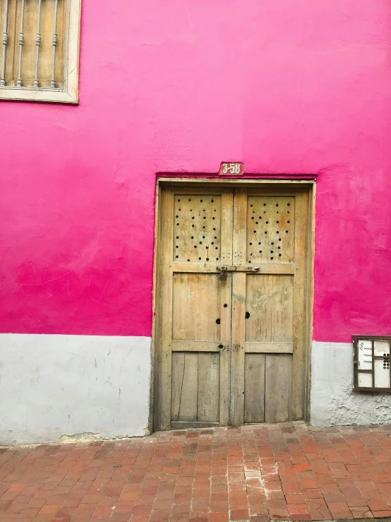 a pink building with a wooden door in front of it, by Gina Pellón, pexels contest winner, quito school, payne's grey and venetian red, three colors, preserved historical, raspberry banana color