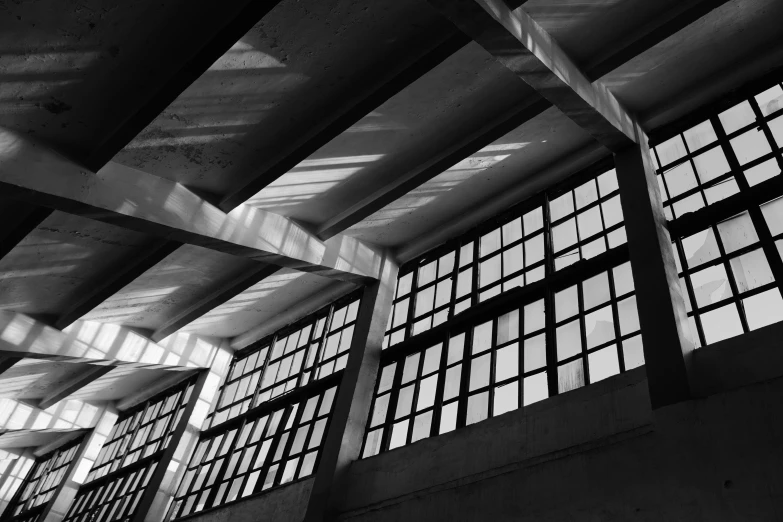 a black and white photo of the inside of a building, a black and white photo, inspired by Alexander Rodchenko, unsplash, brutalism, sunlight shining through windows, tall factory, square lines, low angle photo