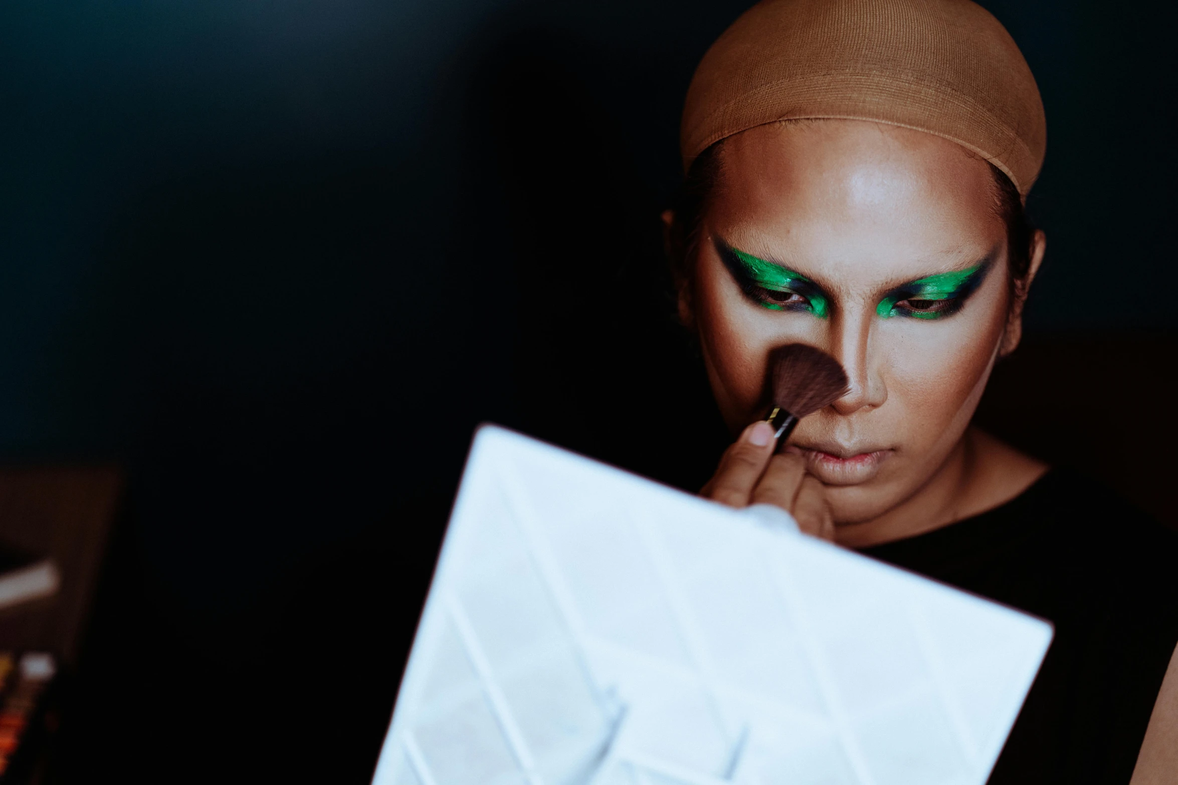 a woman is putting makeup on her face, an album cover, inspired by Aloysius O'Kelly, trending on pexels, green head, futuristic fashion show, androgynous male, nocturnal palette