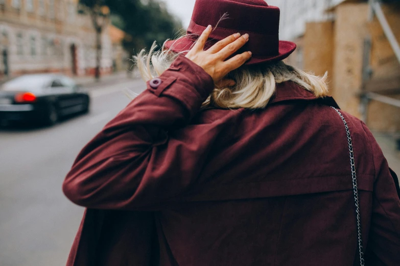 a woman walking down a street talking on a cell phone, a photo, by Emma Andijewska, trending on pexels, maroon hat, with his back turned, red jacket, greeting hand on head