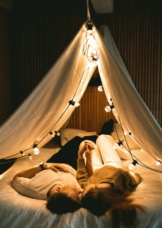 a woman laying on top of a bed under a canopy, pexels contest winner, cabin lights, romantic couple, some bulb lights, teepee