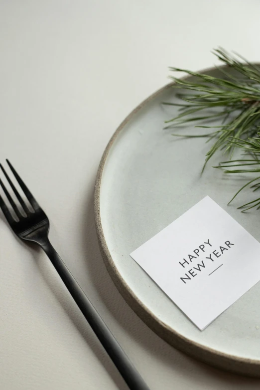 a white plate topped with a piece of paper next to a fork, by Nina Hamnett, trending on unsplash, new years eve, square sticker, bjarke ingels, black fir