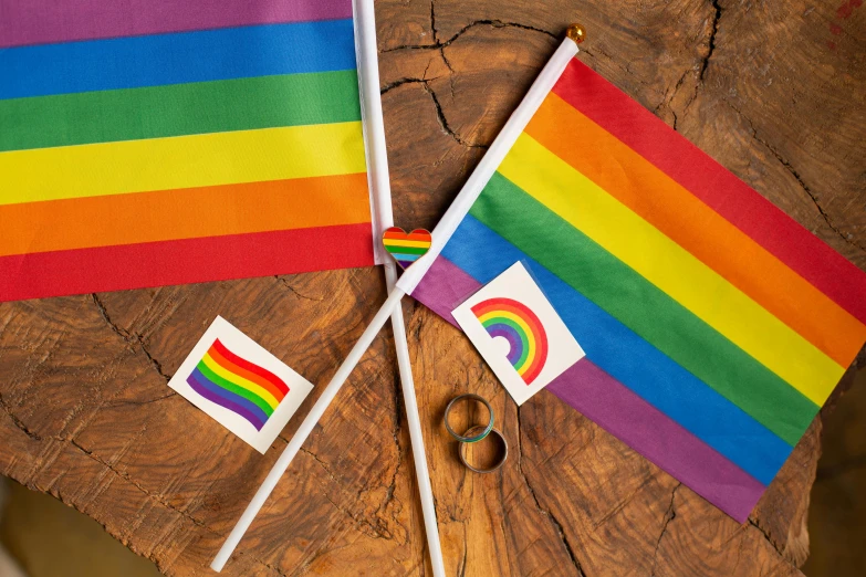 a couple of flags sitting on top of a wooden table, by Helen Stevenson, unsplash, rainbow stripe backdrop, official product photo, various items, closeup of arms