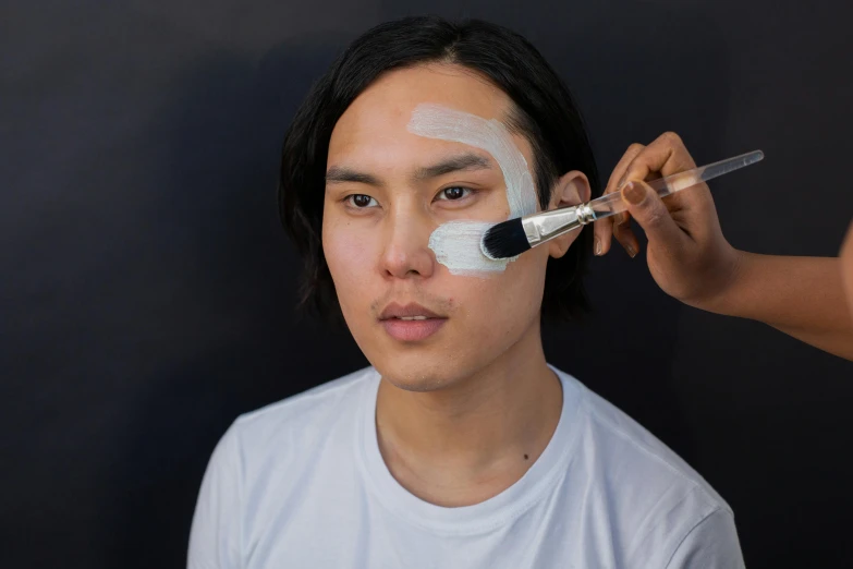 a man getting his make up done with a brush, inspired by Russell Dongjun Lu, white facepaint, clear symmetrical face, half asian, clean face and body skin