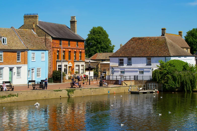 a group of buildings next to a body of water, a photo, arts and crafts movement, gushy gills and blush, old english, thumbnail, small town surrounding