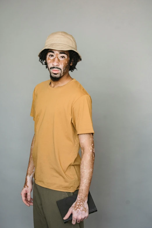 a man standing in front of a gray wall, by Quinton Hoover, bucket hat, wearing a modern yellow tshirt, raw sienna, full product shot