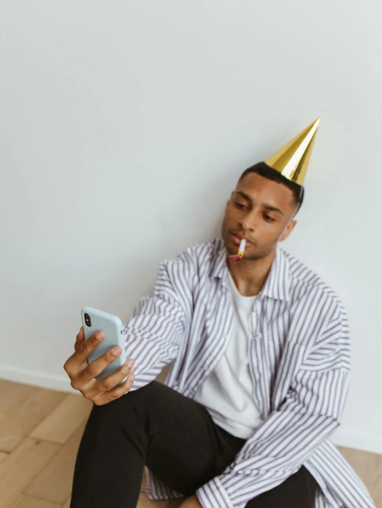 a man in a party hat sitting on the floor, trending on pexels, taking a selfie, non binary model, gold shirt, long nose