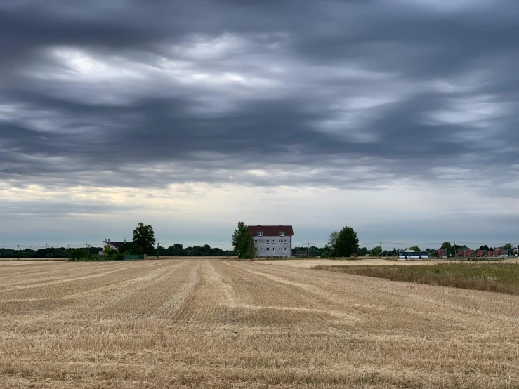 a field with a house in the distance under a cloudy sky, by Karl Pümpin, pexels contest winner, hyperrealism, midwest town, slight stubble, large scale photo, multiple stories