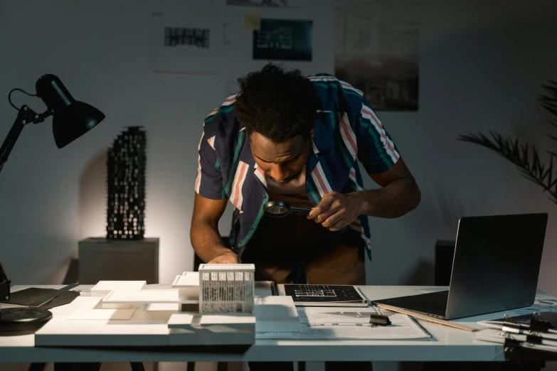 a man sitting at a desk in front of a laptop computer, inspired by Afewerk Tekle, pexels contest winner, hyperrealism, architectural model, low lighting, celebrating, architectural planning