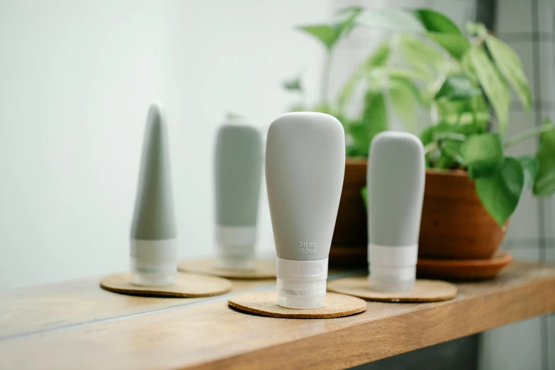 three white vases sitting on top of a wooden table, a picture, inspired by Eero Snellman, purism, silicone cover, gray color, skincare, holding a bottle