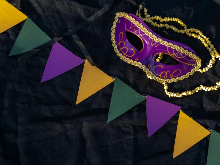 a purple mask sitting on top of a black cloth, inspired by Mardi Barrie, trending on pexels, red pennants, green and gold, background image, yellow and blue ribbons
