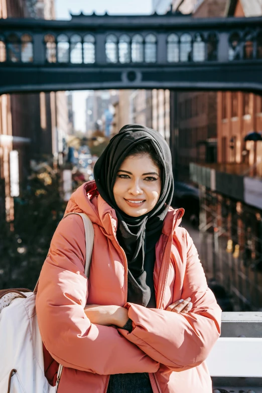 a woman standing on a bridge with her arms crossed, inspired by Maryam Hashemi, pexels contest winner, hurufiyya, wearing a turtleneck and jacket, wearing a head scarf, in the middle of new york, passport photo