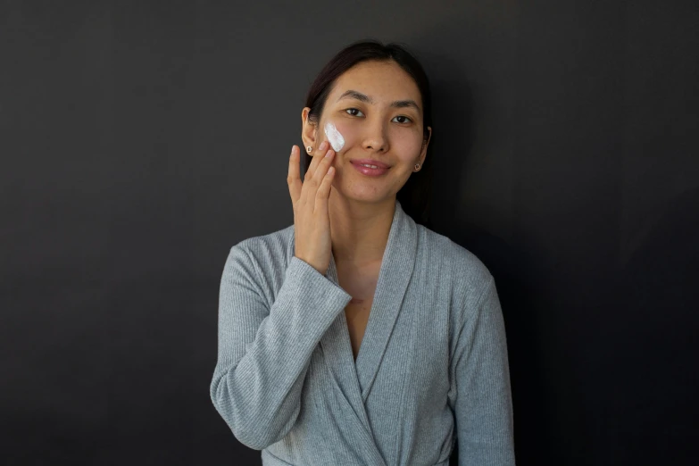 a woman standing in front of a black wall holding a cell phone to her ear, inspired by Ruth Jên, happening, her face is coated in a whitish, japanese collection product, skincare, on grey background