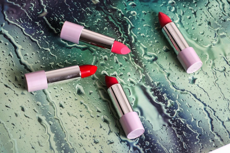 a couple of red lipstick sitting on top of a wet surface, inspired by Luma Rouge, with big chrome tubes, thumbnail, mint, in colour